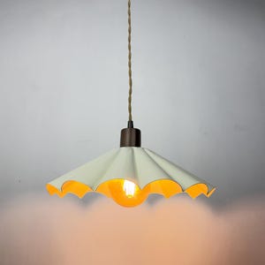 May include: A cream-colored, scalloped pendant light fixture with a warm, orange glow emanating from the exposed bulb. The light has a dark brown base and a twisted, beige cord.