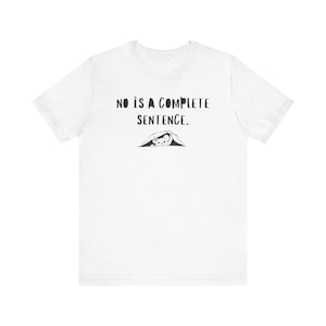 May include: White t-shirt with the text "NO IS A COMPLETE SENTENCE" in black, above a small illustration of a creature under a blanket. The shirt is a casual, everyday wear item.