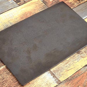 May include: A rectangular, flat, dark brown metal plate with a matte, textured surface. The object features clean, straight edges and a uniform, solid color finish across its entire top surface, presenting a simple and functional design.