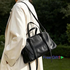 May include: A black leather handbag with a top handle and a shoulder strap. The bag is rectangular and has a zip closure. The image also shows a cream-coloured trench coat.