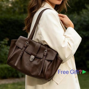 May include: A dark brown leather handbag with a rectangular shape, featuring two front flap closures with buckles and a top handle. The bag has a shoulder strap and a silver-coloured clasp. The bag is worn over a white coat.