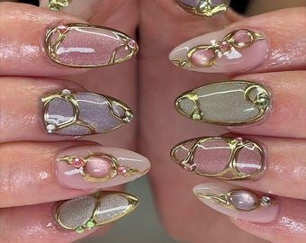 May include: Close-up of a set of manicured nails. Each nail features a different design with a gold metallic outline and various pastel colors, including pink, purple, and gray. Some nails have small, decorative gems.