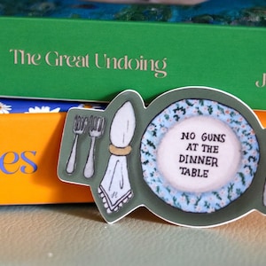 May include: A green and white sticker with a plate and silverware. The plate has a blue and white floral pattern and the text "NO GUNS AT THE DINNER TABLE".