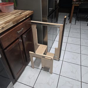 May include: A wooden step stool with a pull-out design. The stool is light-colored and has two steps. It is designed to be pulled out from a cabinet or similar structure. The step stool is made of wood and is designed to provide extra height.