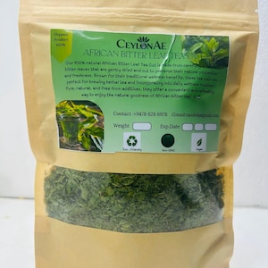 Puede incluir: Una bolsa de papel marrón llena de té African Bitter Leaf Cut verde seco. La bolsa tiene una etiqueta verde con el texto "CEYLONAE AFRICAN BITTER LEAF TEA CUT" y "Organic Product 100%." El té se describe como puro, natural y sin aditivos.
