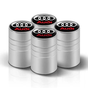 May include: Four silver tire valve stem caps with the Audi logo. Each cap has a black top with the Audi rings logo in white and the Audi name in red. The caps are cylindrical with horizontal grooves.