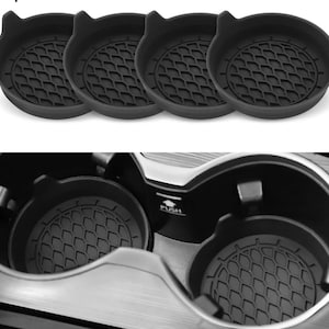 Puede incluir: Cuatro posavasos negros de silicona para coche con diseño de orejas de gato. Los posavasos tienen un patrón geométrico texturizado en el centro. La imagen también muestra los posavasos en los portavasos de un coche.
