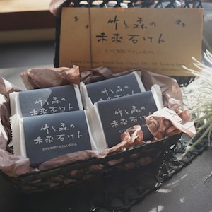 以下が含まれることがあります： 織り込まれたバスケットに、包装された石鹸が入っています。各石鹸には、日本語のテキストが書かれた濃い青色のラベルが付いています。バスケットには、日本語のテキストが書かれた茶色の段ボール箱も入っています。石鹸は白い紙と茶色の薄紙で包まれています。