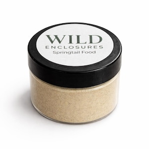 May include: A small, clear glass jar with a black lid, filled with a light brown powder. The jar has a white label with the words "WILD ENCLOSURES" and "Springtail Food" in green lettering.