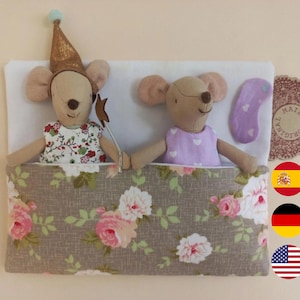 Könnte beinhalten: Zwei Plüschmauspuppen in einem Bett mit einer blumig gemusterten Decke. Eine Maus trägt einen goldenen Partyhut und ein Blumenkleid und hält einen Sternenstab. Die andere Maus trägt ein lila Kleid mit weißen Herzen und eine passende Schlafmaske.