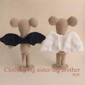 Peut inclure: Deux poupées souris en tissu beige debout. La souris de gauche porte des ailes noires de chauve-souris, et celle de droite porte des ailes blanches avec une rangée centrale de perles. Le texte en bas indique : Clothing big sister/big brother PDF.