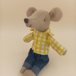 May include: A stuffed mouse toy with light brown fabric, wearing a yellow and white gingham button-down shirt and dark blue denim trousers with cuffed hems. The mouse has large rounded ears, a small dark brown nose, and a stitched mouth.