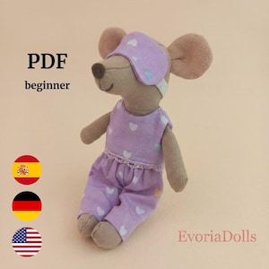 May include: A beige fabric mouse doll wearing a light purple romper with a white heart pattern and a matching purple sleep mask over its eyes. The image includes the text PDF and beginner, along with three circular flag icons and EvoriaDolls.