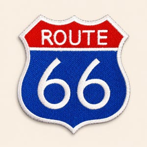 May include: A shield-shaped embroidered patch featuring the text ROUTE in white on a red background above the number 66 in white on a blue background. The entire design is outlined with a white border, creating a classic highway sign aesthetic.