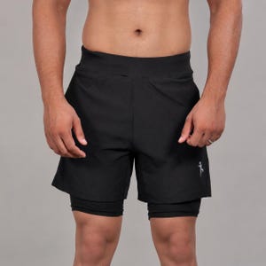 May include: Black athletic shorts with a built-in compression layer. The shorts have a wide waistband and a small, white logo on the left leg. The outer shorts are loose-fitting, while the inner layer provides support. Ideal for running and other sports.