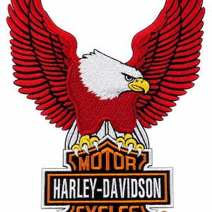 May include: An embroidered patch featuring a bald eagle with bright red wings and a white head, perched atop a black and orange Harley-Davidson Motor Cycles logo. The eagle has a yellow beak and talons, with white and red stitching details throughout.