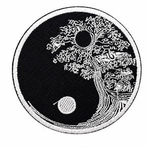May include: A circular embroidered patch featuring a black and white yin yang design. The white section depicts a detailed tree with a circular sun or moon above it, while the black section contains a small white circular dot.