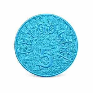 May include: A round, turquoise embroidered patch with the words "LET GO GIRL 5" in a darker turquoise thread. The patch has a textured appearance and is set against a white background.