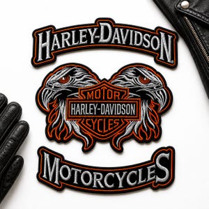 May include: Three embroidered Harley-Davidson patches featuring a top rocker with white text, a central emblem with two eagle heads flanking a shield logo with the text MOTOR HARLEY-DAVIDSON CYCLES, and a bottom rocker with the text MOTORCYCLES.