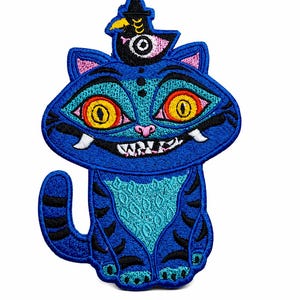 May include: A blue embroidered patch featuring a cartoon cat with a hat. The cat has large yellow eyes, a toothy grin, and black stripes. The patch is designed with various shades of blue and teal.