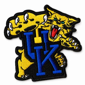 May include: Embroidered patch featuring a yellow wildcat with blue eyes and open mouth, claws extended. The letters "UK" in blue are centered on a black background. The patch is outlined in black.