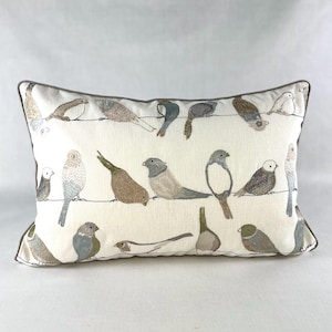 May include: Rectangular decorative pillow with a cream-colored background featuring embroidered birds perched on wires. The birds are in various shades of gray, brown, and white. The pillow has a gray border.