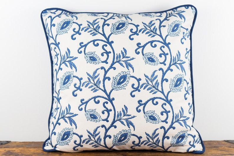 May include: A white throw pillow with a blue floral pattern. The pillow has a blue border.