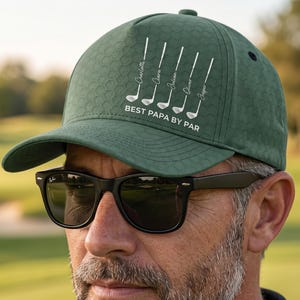 Könnte beinhalten: Grüne Golfkappe mit Wabenmuster. Die Kappe hat weißen Text und Golfschläger-Grafiken. Der Text auf der Kappe lautet "BEST PAPA BY PAR" mit Namen über den Golfschlägern. Die Kappe wird von einer Person mit schwarzer Sonnenbrille getragen.