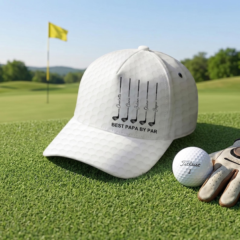 May include: A white baseball cap with a dimpled texture resembling a golf ball. The front features a black graphic of five golf clubs with the names Charlotte, Clara, Julian, Oliver, and Jasper printed vertically, and the text BEST PAPA BY PAR.