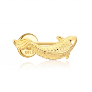 May include: A gold-colored earring in the shape of a koi fish. The earring has a textured body and a round backing with the text "S925". The fish is oriented horizontally, with its tail and fins visible.