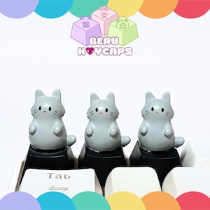 May include: A set of three ceramic mugs with a speckled, matte finish. Each mug features a different color: light blue, cream, and gray. The mugs have a simple, modern design and a comfortable handle.