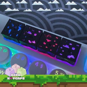 Peut inclure: Gros plan sur un clavier mécanique avec des keycaps personnalisés. Les keycaps sont noirs avec une surface texturée et illuminés de lumières bleues, roses et violettes. Le clavier a un motif de nuages pixélisés en arrière-plan.