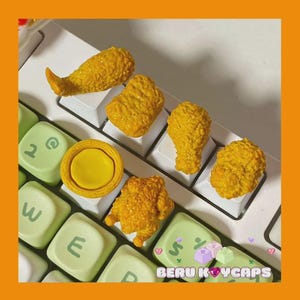 May include: A collection of yellow, fried chicken-themed keycaps arranged on a white keyboard. The keycaps include a drumstick, nuggets, and a chicken patty. The keyboard also features light green keys with white lettering. The brand name "BERU KOYCAPS" is visible.