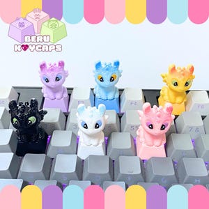 May include: A collection of colorful dragon-themed keycaps on a keyboard. The keycaps are in various colors, including black, purple, blue, white, pink, and yellow. The keycaps are designed with dragon figures and are a fun accessory for any keyboard.