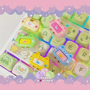 May include: A collection of colorful, cat-shaped keycaps in yellow, pink, green, and blue, resting on a keyboard. Each keycap features a small screen design. The keyboard keys are light green and white. The image has a pastel aesthetic.