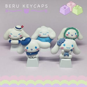 May include: Five white keycaps with cartoon character designs. Each keycap features a different outfit, including a sailor hat, a blue beret, and a green bonnet. The text "BERU KEYCAPS" is at the top. Additional keycaps with square designs are in the background.