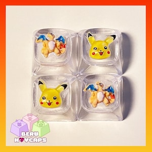 May include: Four clear, square keycaps with cartoon character designs. Two keycaps feature a yellow Pikachu, and two feature a Charizard. The keycaps are arranged in a 2x2 grid. The text "BERU KEYCAPS" is at the bottom.