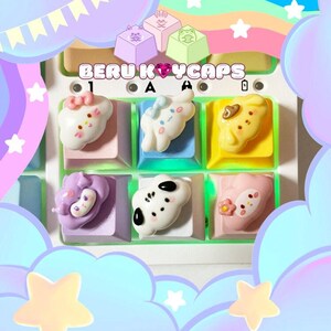 May include: A close-up of a keyboard with custom keycaps. The keycaps are pastel-coloured and feature cute, cartoon-like designs. The text "BERU KEYCAPS" is displayed above the keys. The keycaps have a variety of shapes and colours, including white, yellow, pink, and purple.