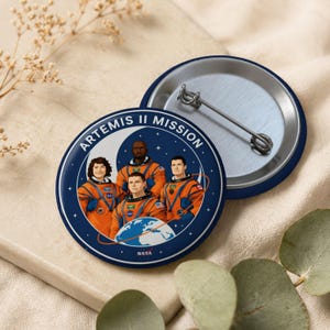 May include: Two blue and silver Artemis II Mission pinback buttons. One button shows a team of astronauts in orange suits, with the text "ARTEMIS II MISSION" and the NASA logo. The other button is a silver pinback.