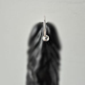 Könnte beinhalten: Ein glattes, mattschwarzes phallisches Objekt mit einem polierten silberfarbenen Metallring an der Oberseite. Das Objekt hat eine texturierte, konturierte Oberfläche mit sichtbaren Rillen und einer abgerundeten Spitze, vertikal ausgerichtet.