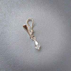 May include: A silver-toned metal earring featuring a smooth, curved hook design and a single, clear, faceted teardrop-shaped crystal bead dangling from a small jump ring. The earring has a polished, reflective finish and a simple, elegant structure.