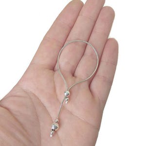 May include: A silver-colored adjustable bracelet with a delicate chain and small, round beads. The bracelet is held in a hand, showcasing its design and details. The bracelet's adjustable feature is visible.