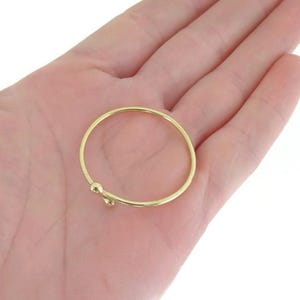 Peut inclure: Une fine bague dorée polie présentant un design simple ouvert. L'anneau est circulaire et lisse, se terminant à une extrémité par un petit détail en forme de perle arrondie qui ajoute une touche subtile à la structure métallique du bijou.