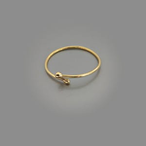 Könnte beinhalten: Ein dünner Goldring mit offenem Design und zwei kleinen, abgerundeten, tropfenförmigen Enden, die sich leicht überlappen. Das Band ist glatt und kreisförmig und weist eine polierte metallische Oberfläche auf, die das Licht reflektiert.