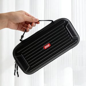 Pode incluir: Estojo de transporte retangular preto com design canelado e alça. O estojo tem um logotipo vermelho e branco que diz "IINE". O estojo é segurado por uma mão.