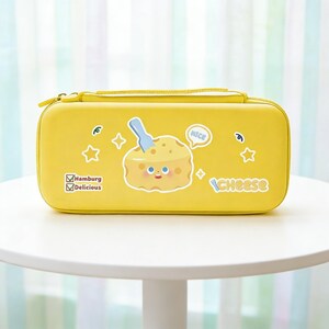 May include: A yellow zippered case with a cartoon cheese graphic. The case has a handle and features the words "Cheese", "Nice", "Hamburg", and "Delicious". Decorative stars and a blue utensil are also present.