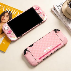 Op de afbeelding: Roze handheld gameconsole met een zwart scherm, met een dambordpatroon op de achterkant en decoratieve knoppen. De voorkant heeft een wit en roze ontwerp met een cartoonkonijn en pootafdruk. Het woord "GAME" is zichtbaar.