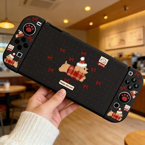 May include: Black Nintendo Switch case with a festive dog design. The case features a repeating pattern of red bows and polka dots. A cartoon dog wearing a Santa hat and plaid coat is centered on the case. The text "Happy new year" is also visible.