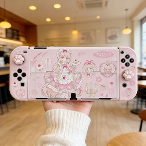 Op de afbeelding: Een roze Nintendo Switch-hoesje met een anime-achtige illustratie. De hoes heeft roze pootafdruk-joysticks en -knoppen. Het ontwerp bevat een meisje, cupcakes en Japanse tekst.