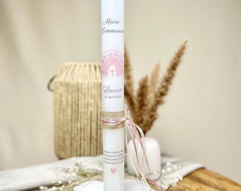 May include: A white communion candle with pink and gold accents. The candle features the text "Meine Kommunion" and the name "Leonie" with the date "05. April 2023". It is decorated with a pink rainbow and a cross.
